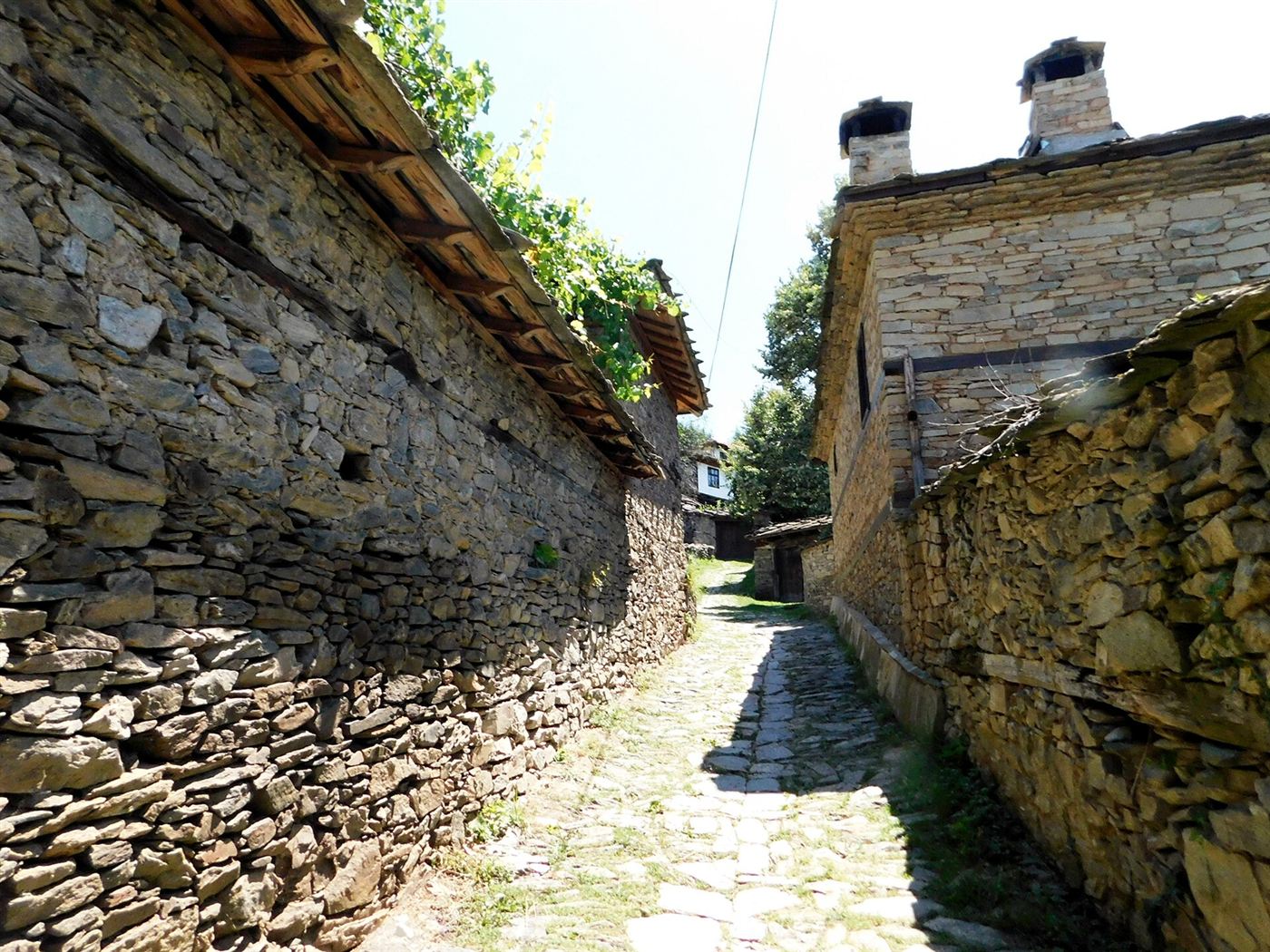 A cobbled lane in Leshten between dry-stone walls, stone chimneys on the roof above