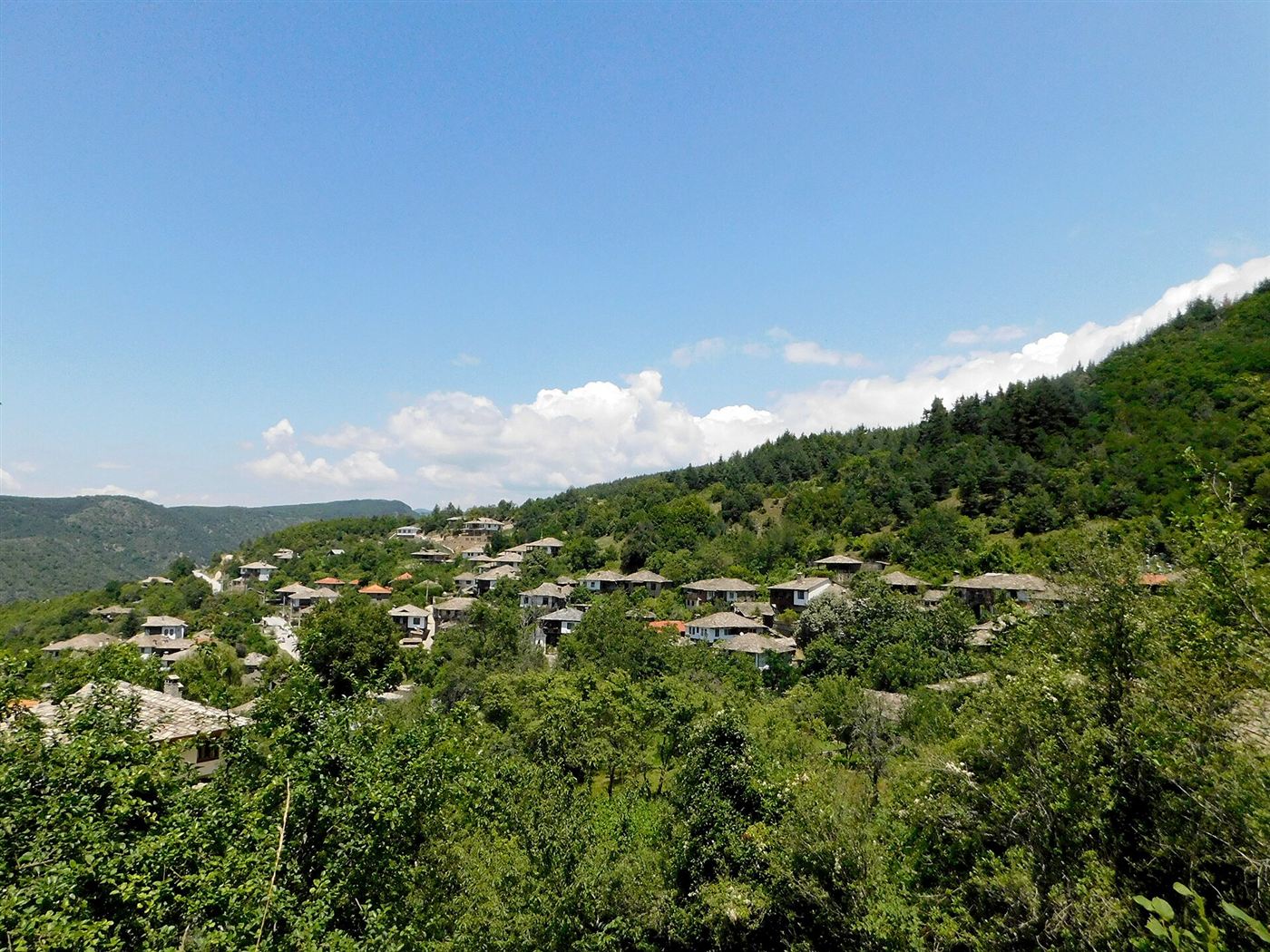 Leshten’s houses scattered on a wooded mountainside under a blue sky